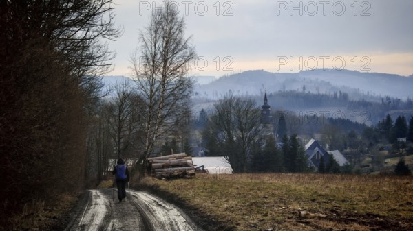 Rural trail leads to a small village with a church in the background, surrounded by hills, Thuringian Forest nature park Park