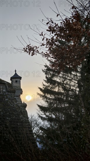 A castle tower, bay window of a fortress wall rising into the sky, surrounded by trees at sunset, Franconian Forest nature park Park
