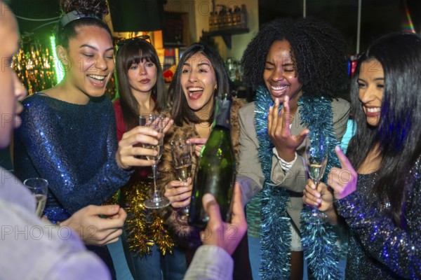 Group of excited diverse young adult friends smiling and laughing while celebrating a special event, enjoying a bottle of champagne and sparkling drinks at a lively party
