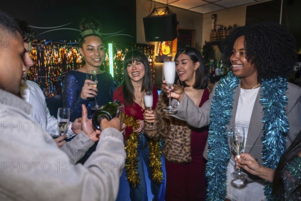 Diverse friends celebrating indoors with festive decorations as one man pours champagne into glasses, a joyful multi ethnic group toasting and enjoying a stylish evening together
