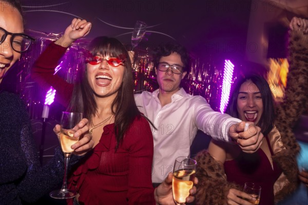 Young diverse friends dancing and cheering while holding glasses of alcoholic drinks, enjoying a lively nightlife party with exciting purple neon lights and a vibrant atmosphere