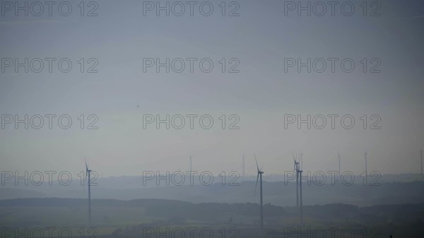 Blurred range of hills with isolated wind turbines in morning fog under blue sky, Franconian Forest nature park Park