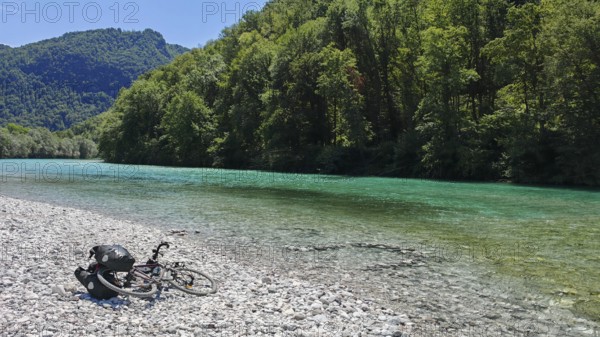 Bicycle lying next to a clear river on a pebble beach surrounded by forest, Soca Valley, Slovenia
