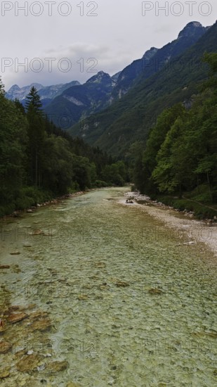 Long river with gravel bed surrounded by wooded mountains under a cloudy sky, Soca Valley, Slovenia