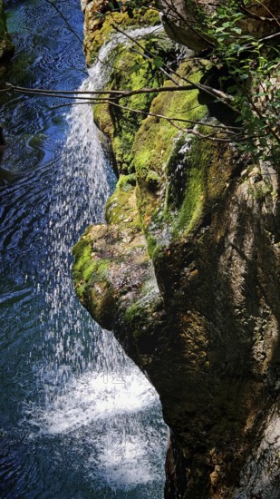 Waterfall runs over moss-covered rocks and splashes into a blue pool, Soca Valley, Slovenia