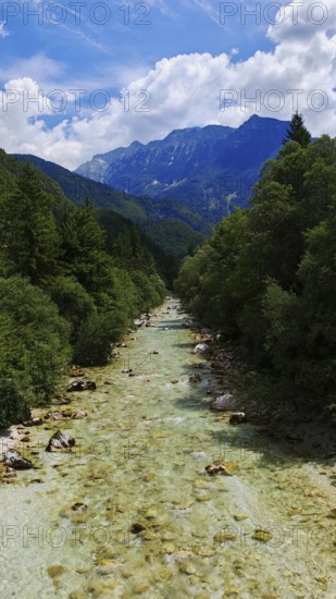A clear river flows through a wooded mountain landscape under a blue sky, Soca Valley, Slovenia
