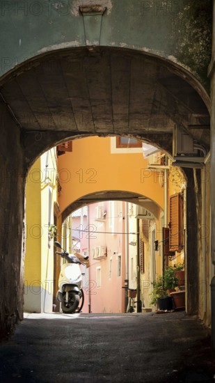 Narrow passageway in an old town with various colorful buildings and a scooter, Slovenia
