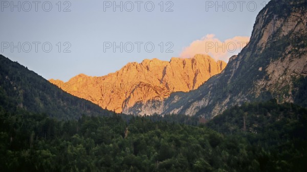 Mountains at sunset with impressively illuminated rocks and dark forest in the foreground, Slovenia