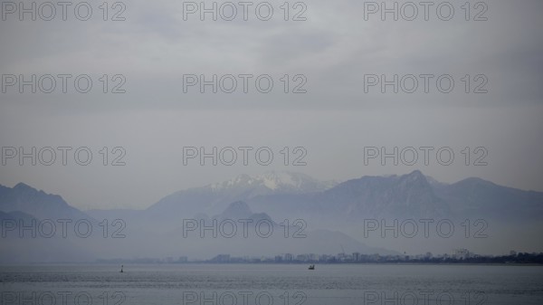 Blurred mountains and a distant city in fog over a calm sea with boats, Antalya, Turkey