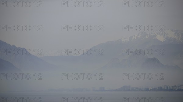 Blurred mountains rise above the misty sea under a grey sky, Antalya, Turkey