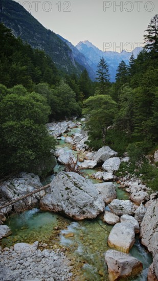 A clear mountain river surrounded by rocks and trees with mountains in the background, Soca Valley, Slovenia