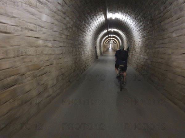 A cyclist crosses a long, illuminated stone tunnel, Slovenia