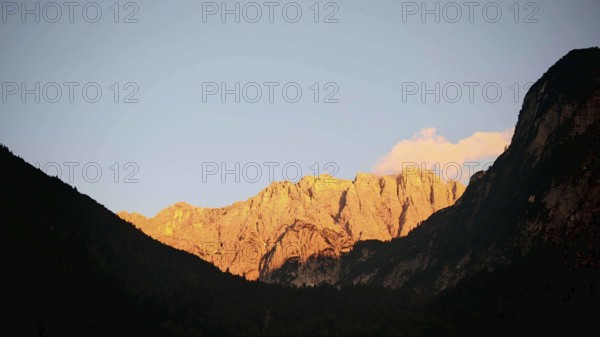 Mountains at sunset with golden light on rocks and dark silhouette of a mountain, Slovenia