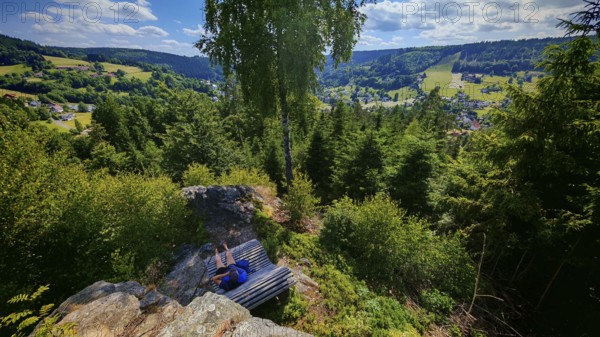 A panorama from a viewpoint with a person on a bench with a view of a picturesque valley, Franconian Forest nature park Park