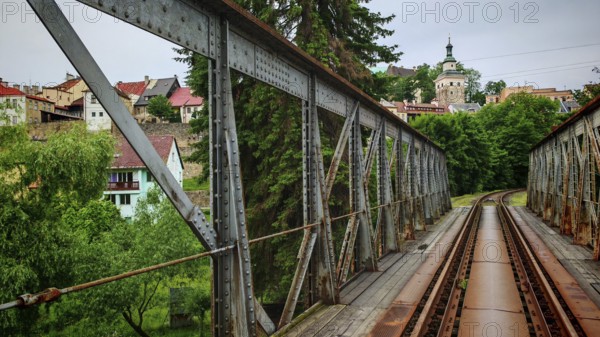 Metal railway bridge leads across a river to a small town with green surroundings, Loket, Czech Republic