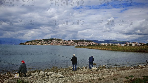 Fishermen on the shore of a lake with a view of a city in the background under cloudy sky, Ohrid, North Macedonia