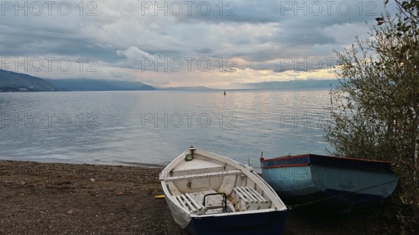 Two abandoned boats on the shore of a lake with mountains in the background under a cloudy sky, Lake Ohrid, North Macedonia
