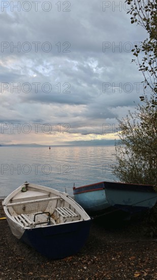 Two boats are lying on the shore of a calm lake under a cloudy evening sky, Lake Ohrid, North Macedonia