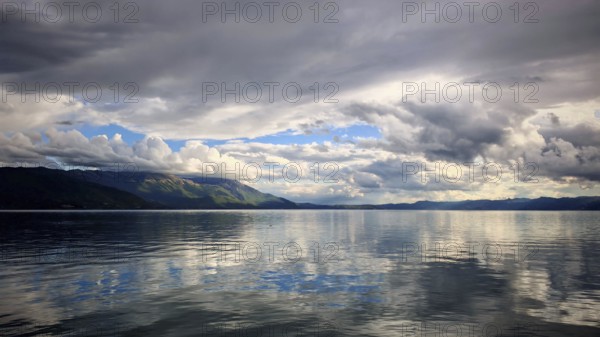 Extensive lake with reflective, dramatic clouds and calm water and mountains in the background, Lake Ohrid, North Macedonia