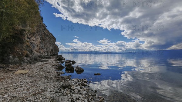 A peaceful rocky coast with a lake whose water reflects the clouds of the dramatic sky, Lake Ohrid, North Macedonia