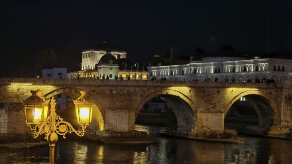 Illuminated bridge at night over a river with historic architecture, Skopje, North Macedonia