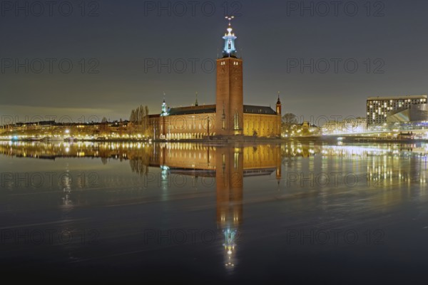 Night scene of a town hall with illuminated tower, peaceful reflection on calm water, Nobel Prize, City Hall, Stockholm, Sweden