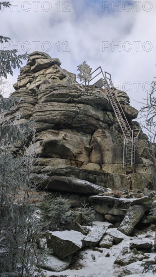 Rock formation with metal stairs in snow surrounded by a wintry sky, Fichtelgebirge