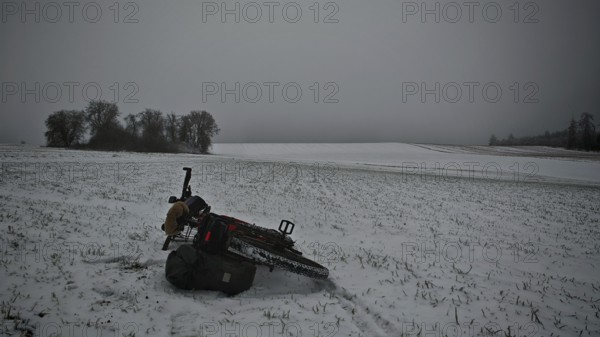 Bicycle lying in the snow on a field with trees in the background under a grey sky, Frankenwald nature park Park, Rennsteig