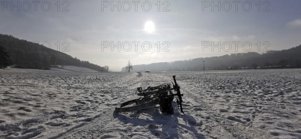 Cycling in the snow on a wide area with rolling hills in the background under the sun, Frankenwald nature park Park, Rennsteig