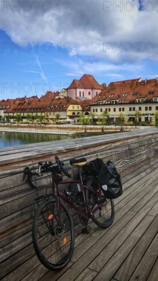 Bicycle on a bridge across a river with historic buildings in the background under cloudy sky, Maribor, Slovenia