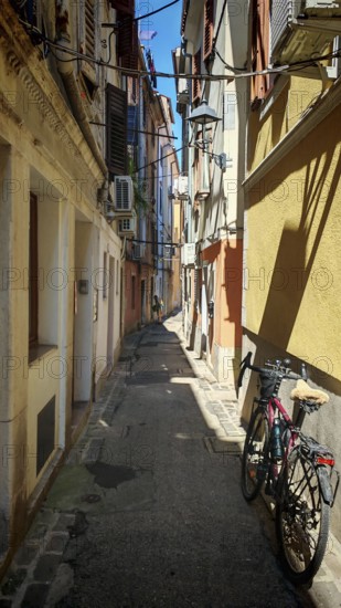 A bicycle is parked in a narrow sunny alley between old buildings, Slovenia