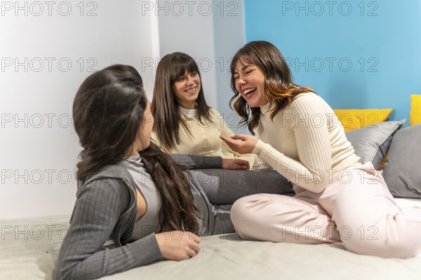 Three young women friends relaxing on a couch, sharing a joyful conversation and laughing loudly, celebrating togetherness and connection in a casual home setting