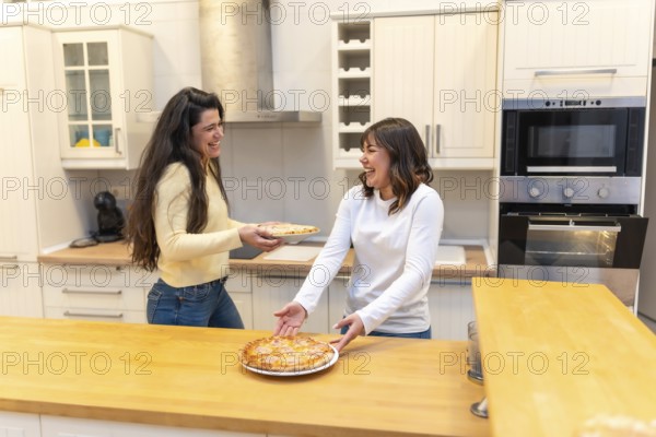 Two cheerful women are happily sharing a delicious homemade pizza in a modern kitchen, enjoying a fun cooking experience and spending quality time together