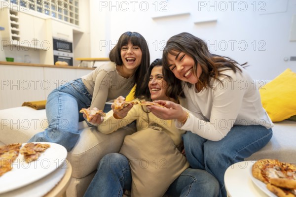 Friends gathered on a cozy sofa enjoying pizza, laughing and sharing slices during a relaxed indoor hangout, capturing genuine joy, friendship and casual weekend fun