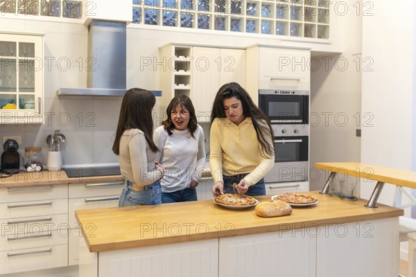 Three young women in a modern kitchen preparing homemade pizza, chatting and laughing while bonding over food, relaxed weekend cooking and shared meal preparation at home