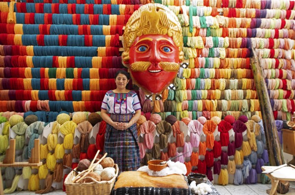 Maya woman, 42 years old, next to a mask of a Moro or Moor for the traditional mask dance, behind a wall full of colorful cotton, traditional crafts in a woman's cooperative, San Juan la Laguna, Atitlán, Sololá Department, Guatemala