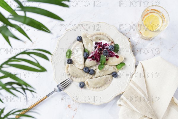 Handmade dumplings filled with sweet ingredients, arranged beautifully on a white plate, topped with berry sauce, fresh blueberries, and mint leaves, ready to enjoy