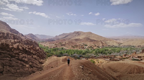 A hiker enjoys the view of a barren mountain landscape with a village in the distance, Morocco