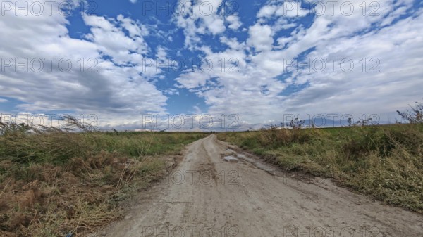 A lonely dirt road leads through a vast landscape under a dramatic cloudy sky, Armenia