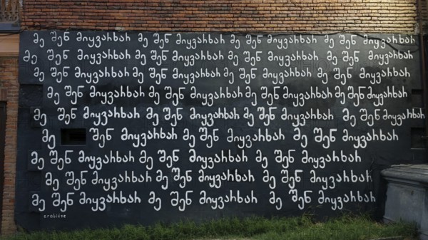 A wall that stands in white letters on a black background in McHedruli writing Ich liebe Dich, against a brick background, Georgia