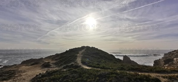 A trail leads over a hill, the sun shines over the coast, Southwest Alentejo nature park Park and Costa Vicentina, Portugal