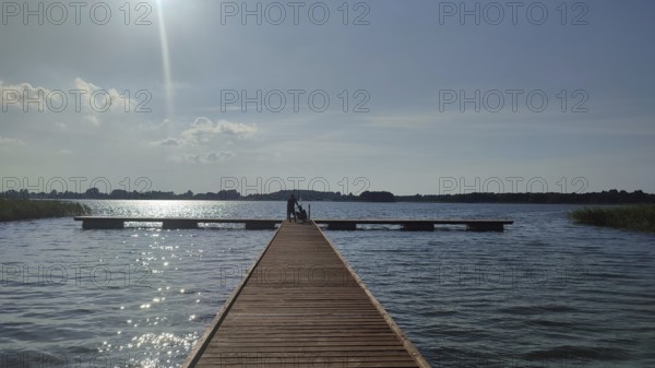 A long wooden walkway leads across a calm lake under bright sunlight, Masuria, Poland