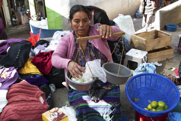 Mayan woman in traditional clothing weighs with a hand scale at the market in Sololá, Highlands, Sololá Department, Guatemala