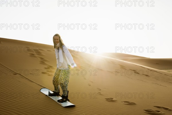 Young woman with snowboard in the sand dunes, near Merzouga, Meknès-Tafilalet region, Erg Chebbi, northern Sahara, Morocco
