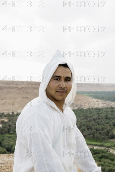Young man and oasis in the background, near Merzouga, Meknès-Tafilalet region, Erg Chebbi, northern Sahara, Morocco