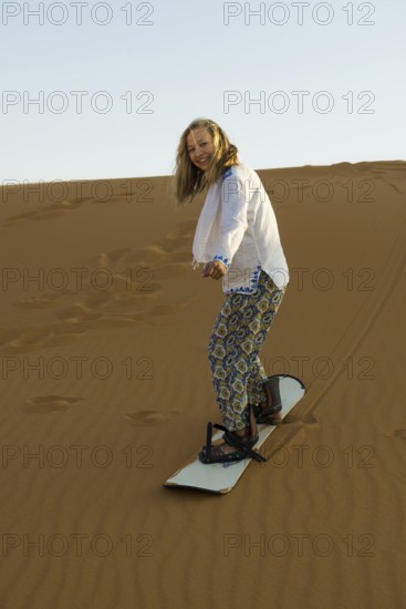 Young woman with snowboard in the sand dunes, near Merzouga, Meknès-Tafilalet region, Erg Chebbi, northern Sahara, Morocco