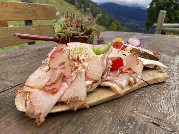 Typical snack on the alpine pasture, bacon bread and cheese bread on wooden plate on wooden table, Halsalm, Ramsau, Bavaria, Germany