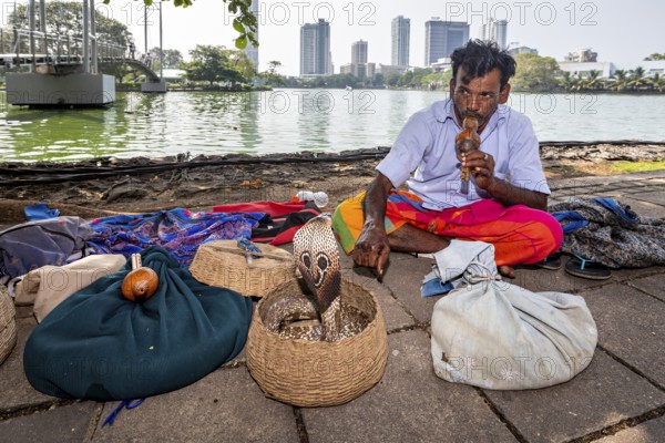 Man playing a wind instrument in front of baskets on the riverbank with an urban background