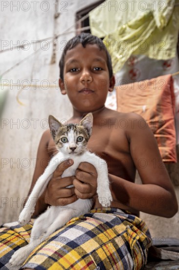 Topless boy proudly holds a cat and smiles in an interior
