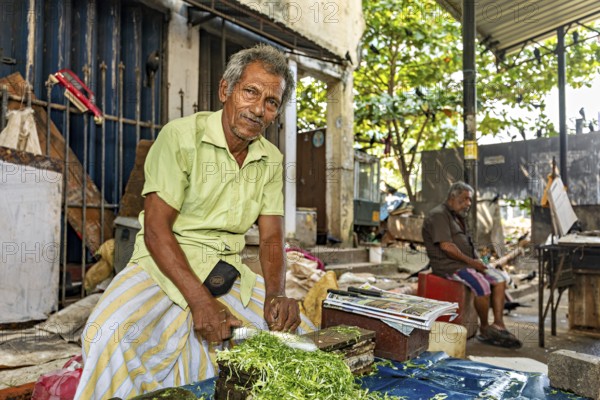 Elderly man cuts vegetables at a street market in an urban setting
